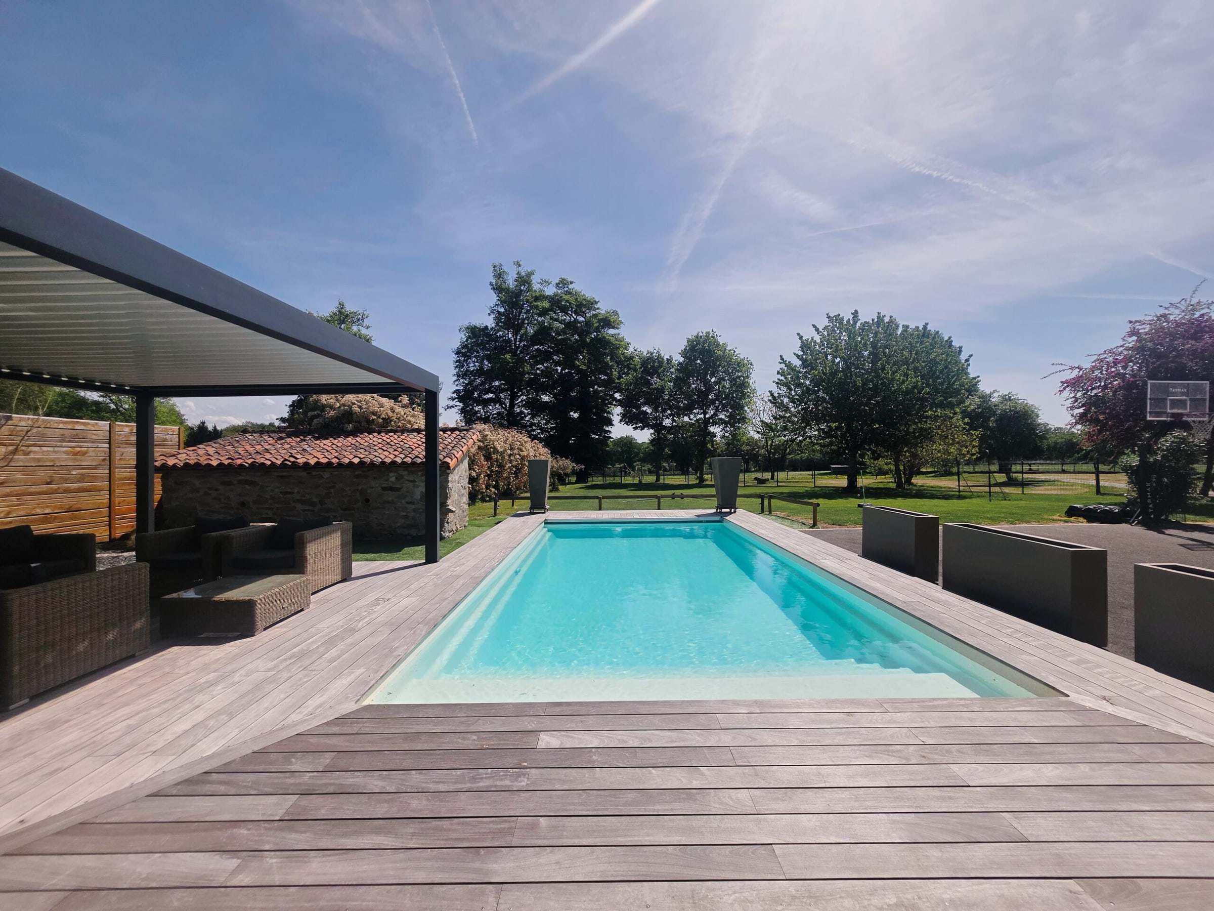 Piscine extérieure bordée de sa pergola sous un ciel bleu