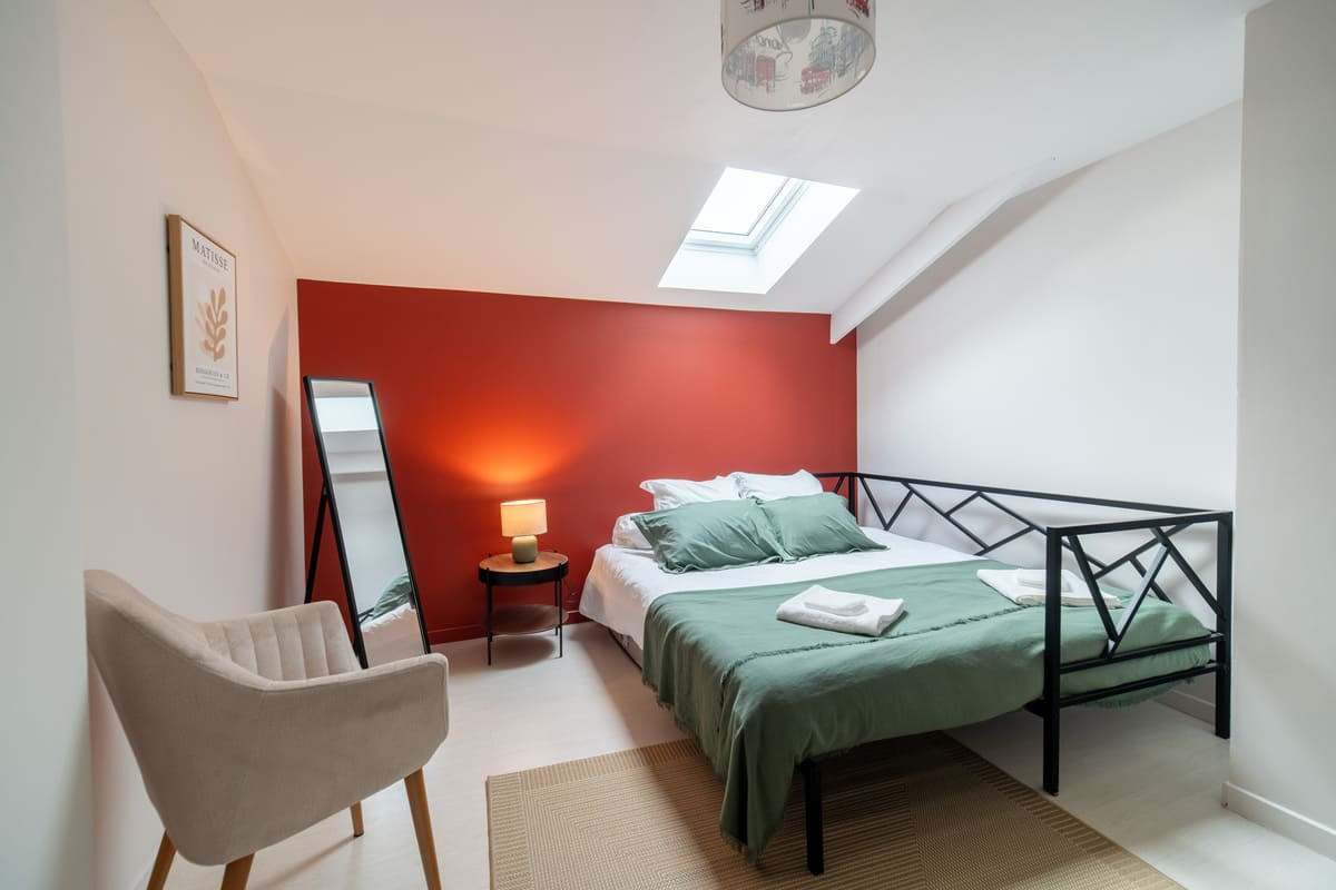 Chambre mansardée au mur rouge avec miroir et fauteuil
